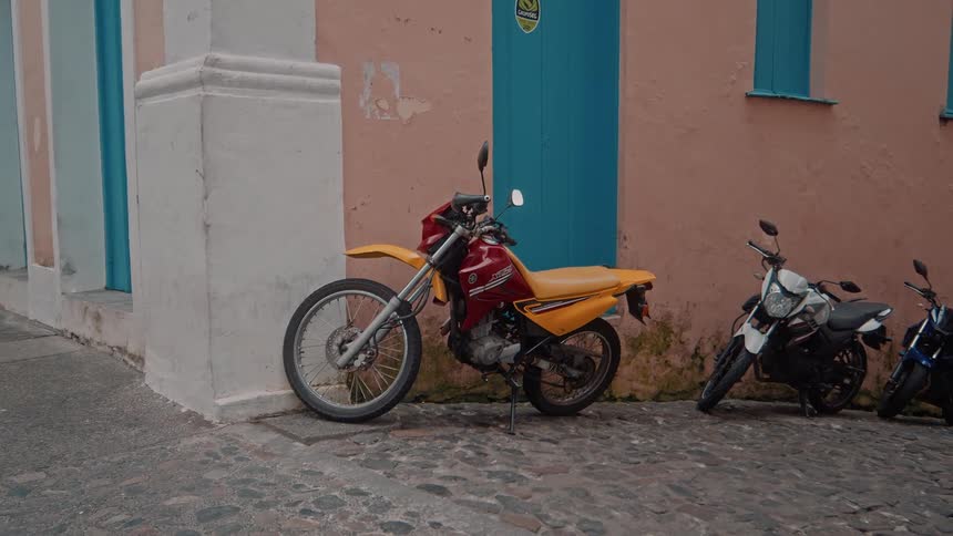 A yellow and red motorcycle is parked next to others on a cobblestone street in front of a colorful building with a blue door