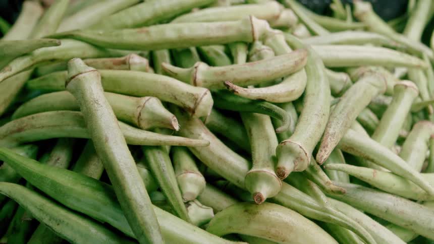 A static closeup shot displays a large pile of fresh green okra pods at a market or grocery stand