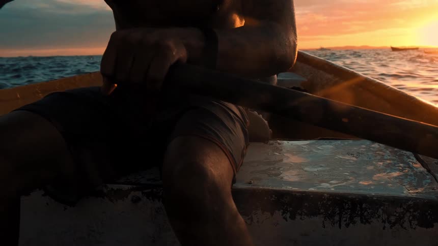 Two people paddle a canoe in the middle of the ocean as the sun rises