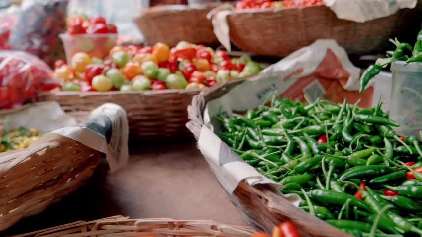 A closeup shot pans across woven baskets filled with fresh green and red chili peppers for sale at an outdoor market stall