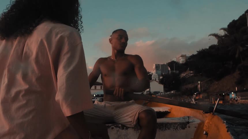 Shirtless man rows boat at sunset with woman seated ahead