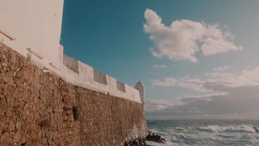 Waves crash along the coast where the wall of a building protrudes