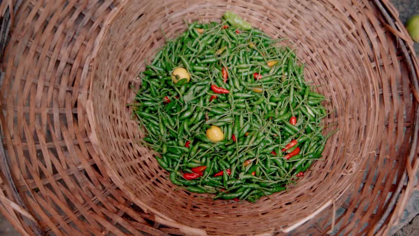 A basket of freshly harvested and colorful chili peppers is displayed for sale at a market in a larger nested woven basket