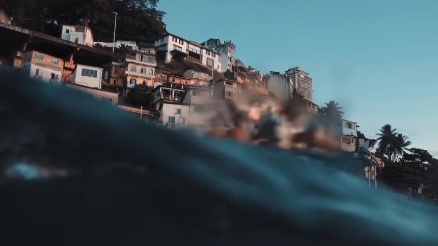 Man rowing a woman in a boat in front of a hillside full of small more primitive houses