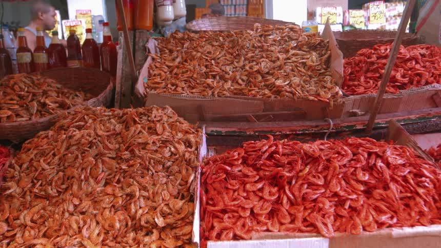 A market with several boxes full of reddish colored shrimp on display