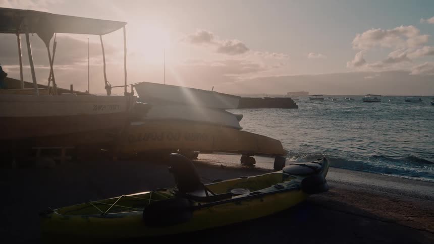 A canoe and a larger boat sit on the shore of a beach near the ocean