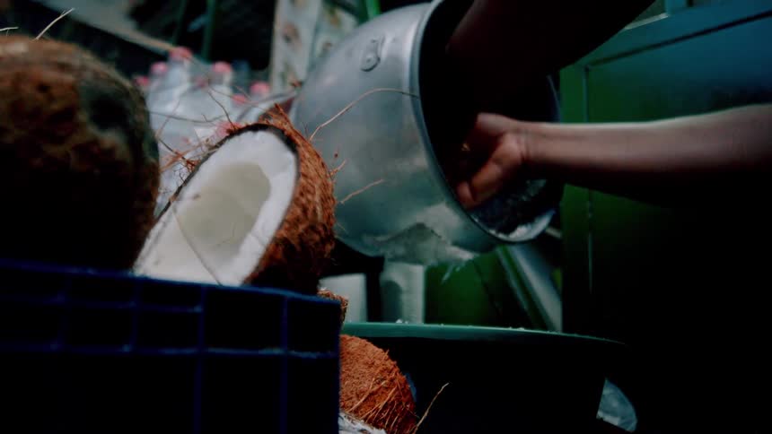 A street vendor grating coconut withmachine in a market setting