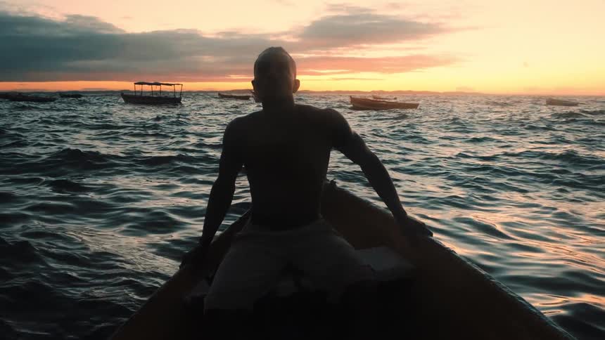 The sun sets as the man sits on the boat