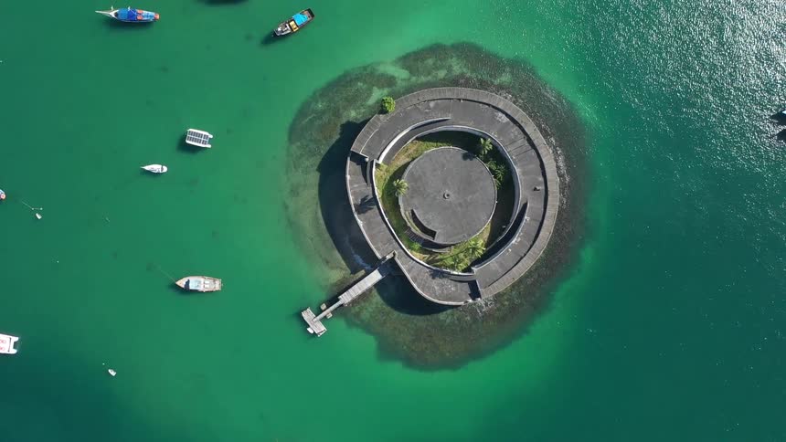 Aerial view of a circular island fortress surrounded by turquoise water and docked boats