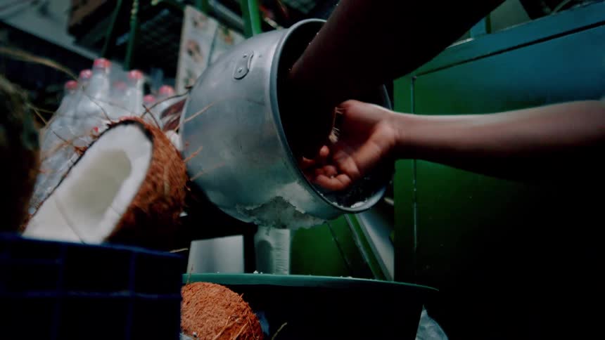 A person is grating fresh coconut using a handoperated grater