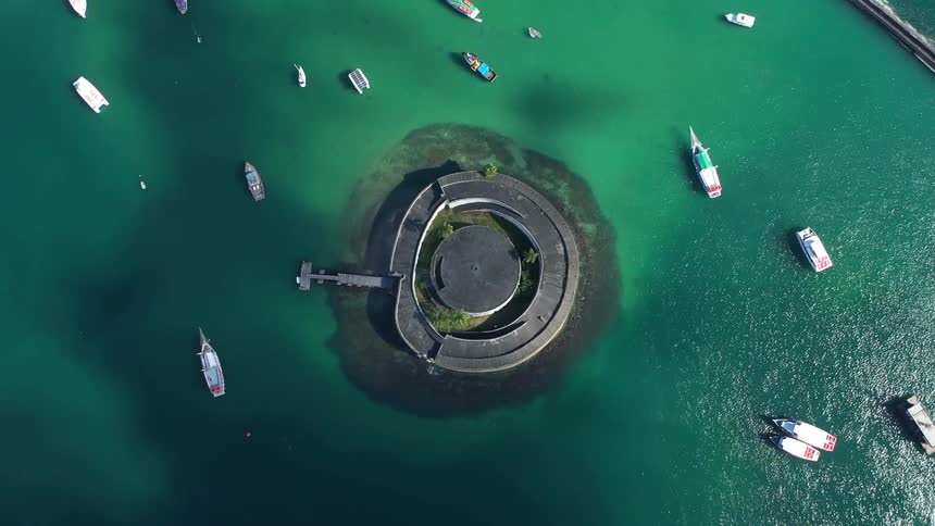 A series of boats float on a lake with green water surrounding a structure in the middle