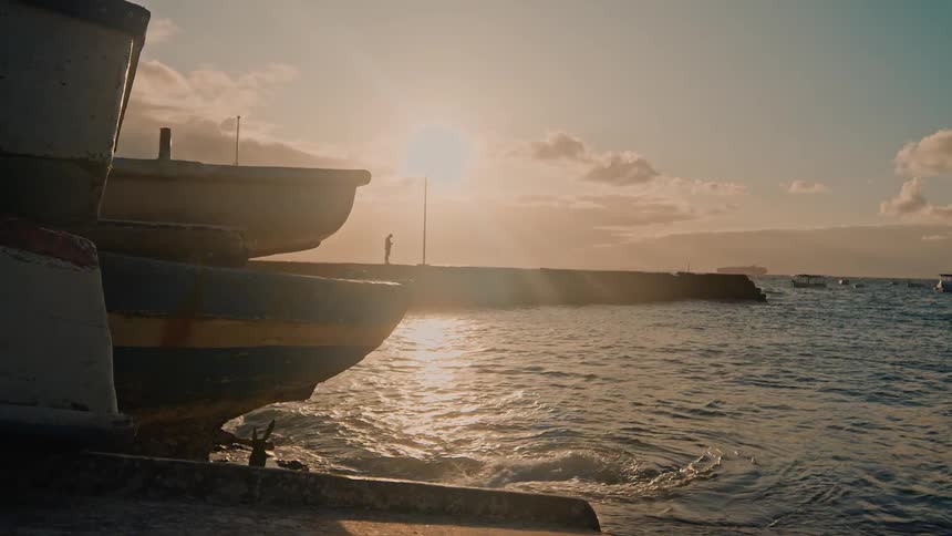 Boats rest by the shore as the sun sets over the ocean
