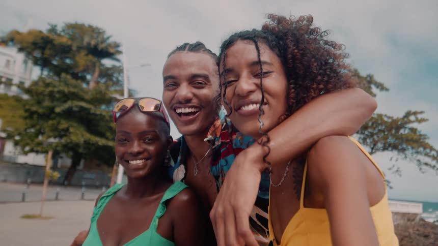 Close up of a group of black friends laughing while preparing to take a selfie on walkway outdoors during daytime