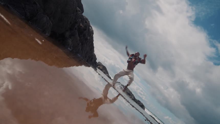 Young black man leaps while standing at the beach during daytime