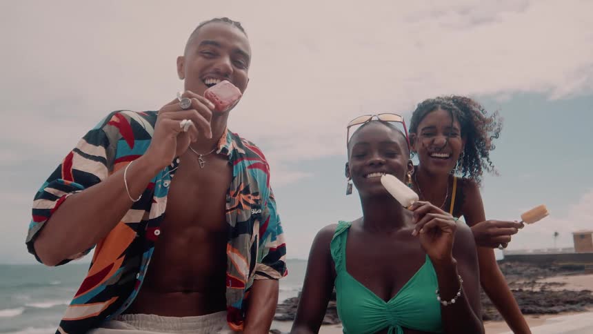 Three friends pose and laugh while eating ice cream at the beach