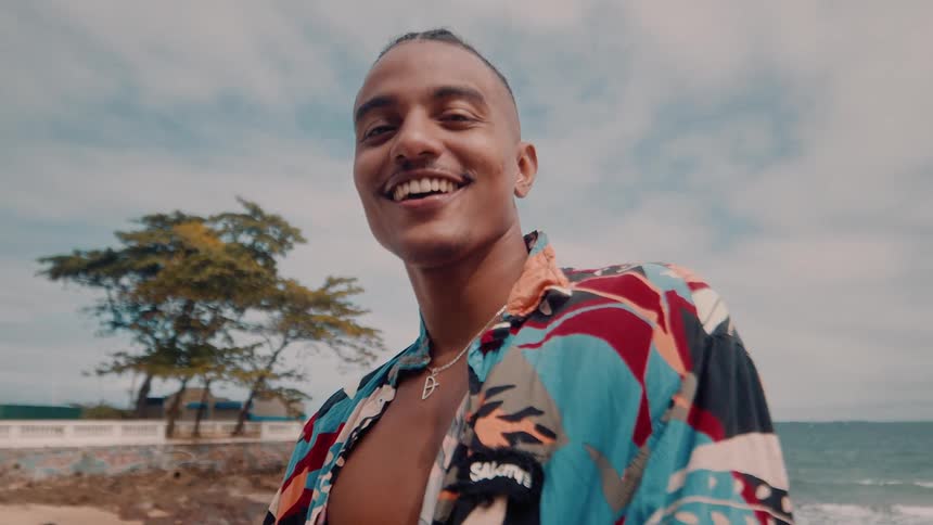 Close up of a young black man smiling while standing outdoors at the beach during daytime