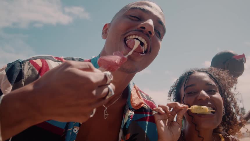 A man and two young women joyfully lick popsicles and enjoy themselves on a sunny day