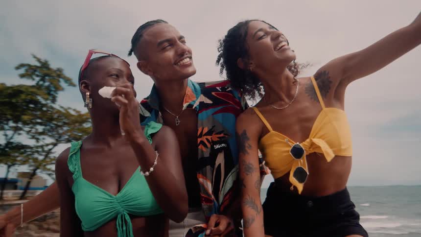 Three friends pose for a cheerful selfie by the ocean on a sunny day