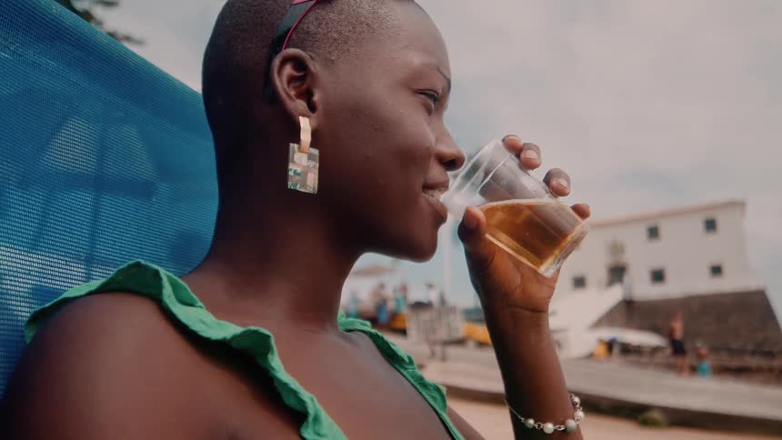 A woman is relaxing and drinking a beverage while sitting at the beach