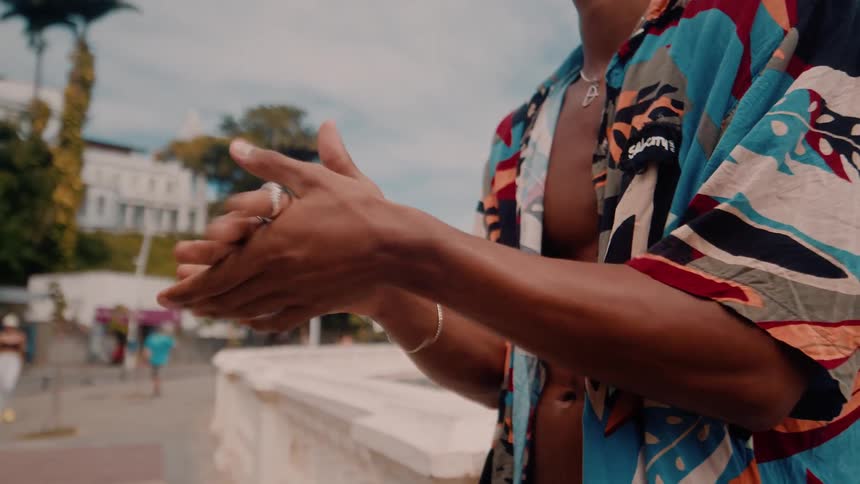 A man in a beach shirt is standing outdoors and clapping his hands