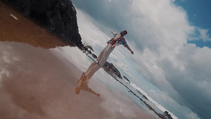 Young black man spreads his arms and turns from side to side while standing at the beach during daytime