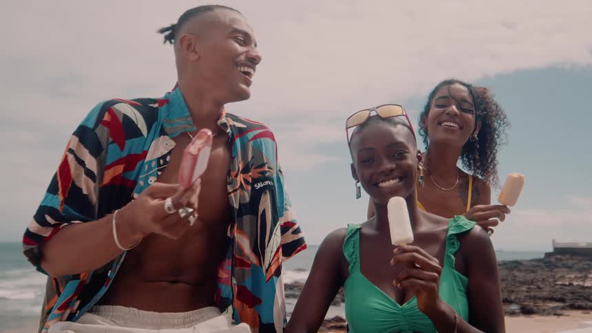 Three friends enjoy popsicles and laugh together by the beach on a sunny day