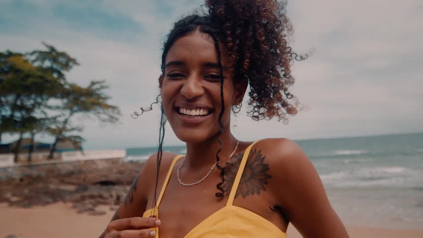 A joyful woman smiles brightly while standing on a beach with the ocean behind her