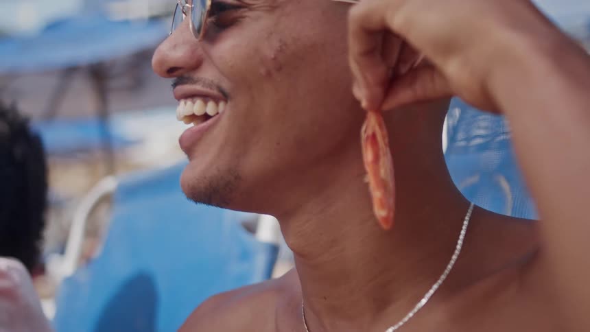 A man sitting on the beach holds an earring up to his ear
