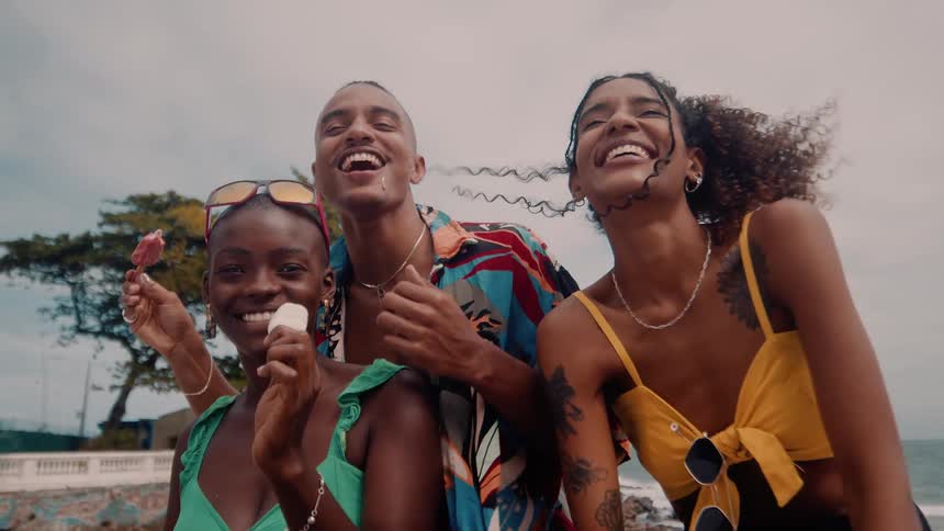 Three friends smile and laugh while enjoying ice cream on a beachside outing