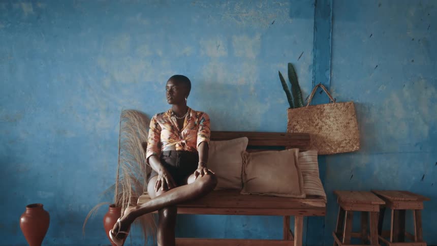 Black african woman poses while sitting on a wooden furniture indoors