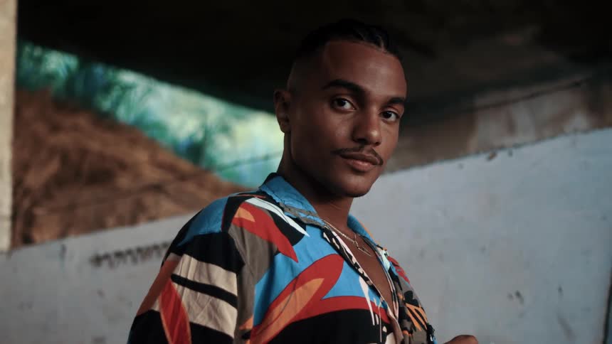 Close up portrait of a young black man buttoning his shirt while standing indoors during daytime