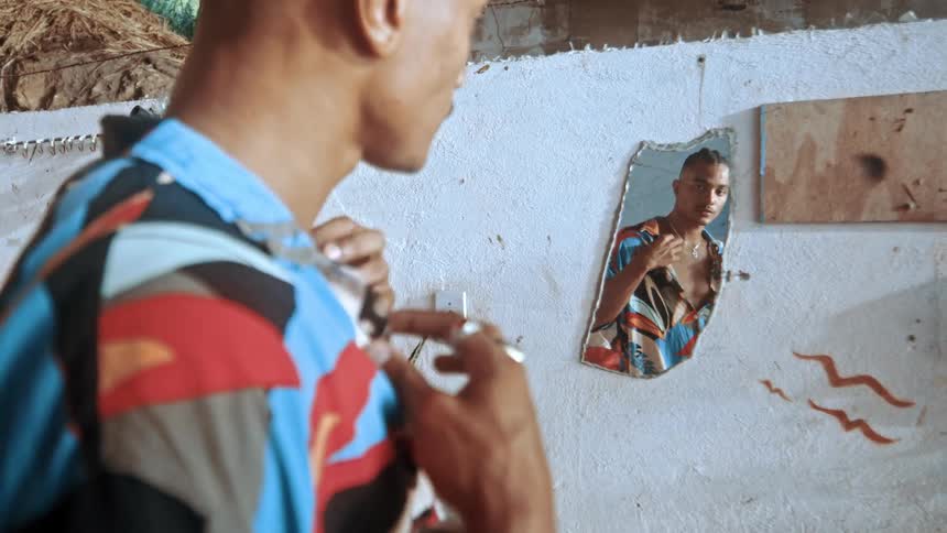 A young black man wearing a summer shirt checks himself out in a mirror adjusting his appearance with a confident and satisfied expression