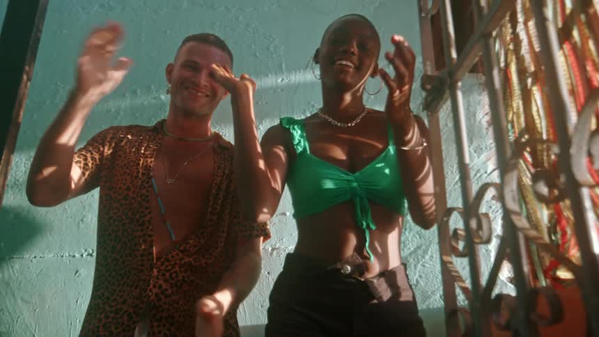 Two people dance joyfully in bright sunlight near a tealcolored wall