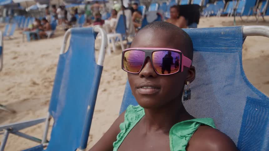 A young black woman wearing sunglasses relaxes on the beach on a sunny day