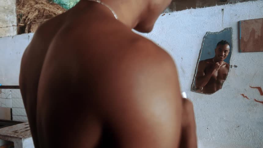 A man is looking at himself in the small piece of mirror on the wall