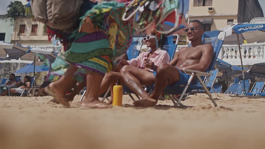 Three friends relax on beach chairs under umbrellas enjoying drinks on a sunny beach