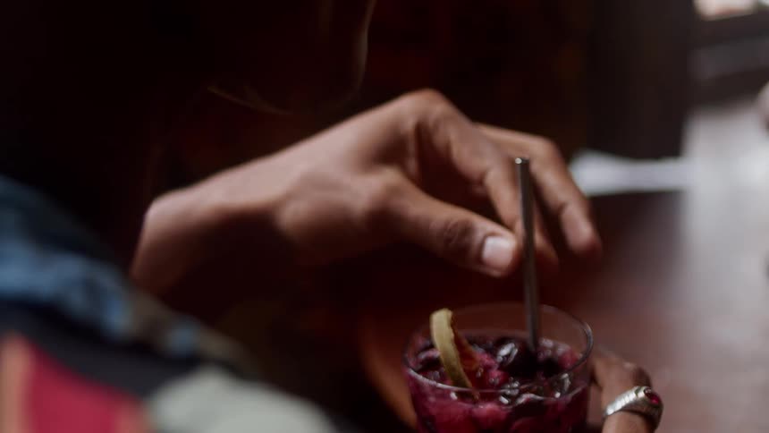 A person stirs a glass of berry drink with a straw while seated at a table