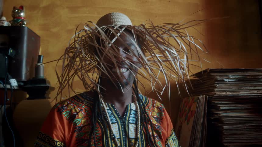 Close up portrait of a black man wearing a straw hat smiling while sitting in a room