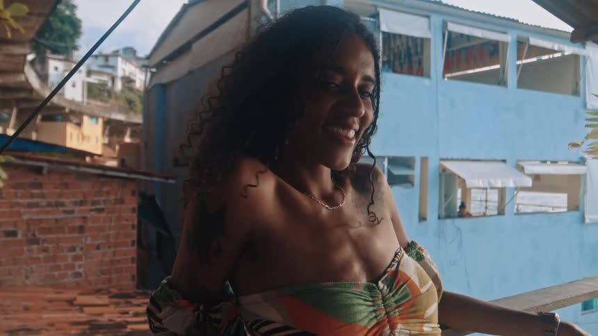 A young woman sits at a resort smiling warmly as the midday sun illuminates her relaxed and cheerful expression