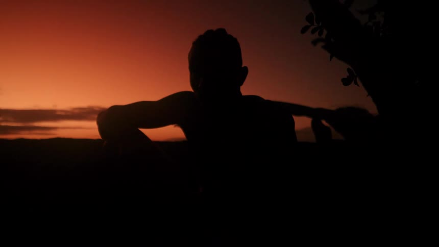 Man sitting outdoors at night is silhouetted against a red sky