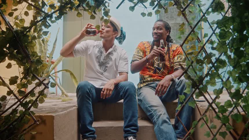 Two men sit on outdoor steps drinking and relaxing in a leafy courtyard