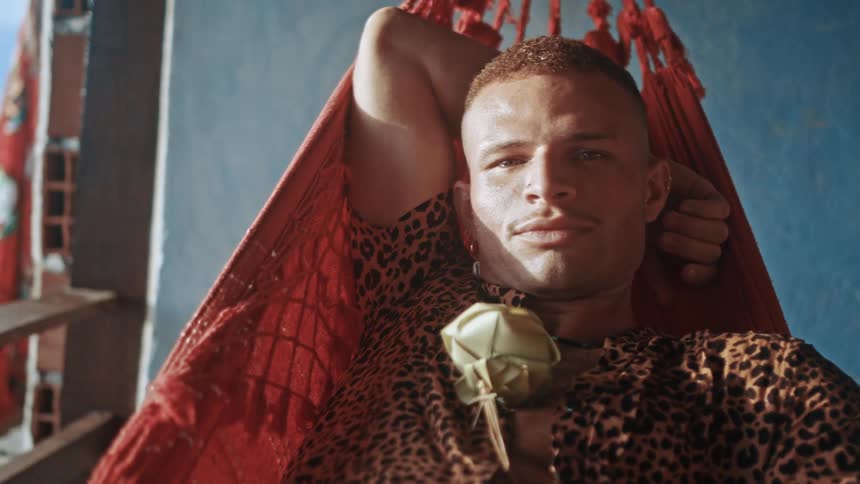 The face of a man who is swinging in a hammock and he is smelling a green plant that is on his lap