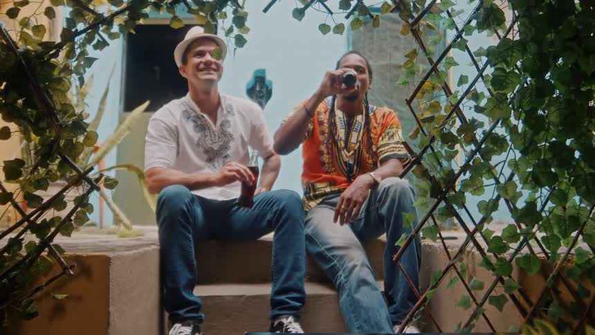 Two happy men are sitting on a step of a staircase and one of them is drinking a beer from a bottle