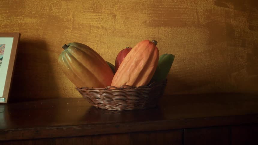 A woven basket holds various colorful gourds on a wooden surface against a textured golden wall