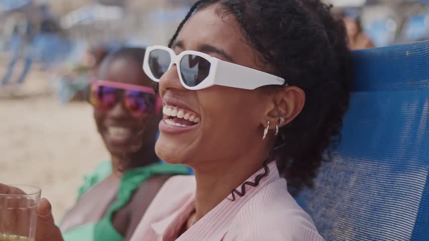 Two women sit in chairs on the beach while laughing