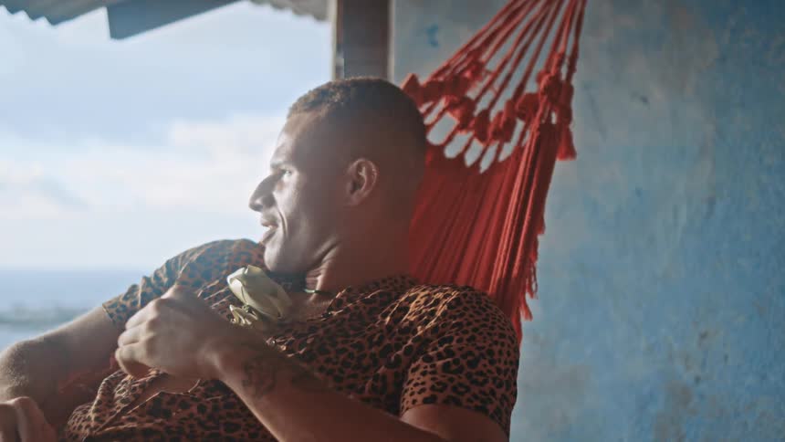 Man relaxes while lying back in a swaying hammock on a covered porch in a coastal building