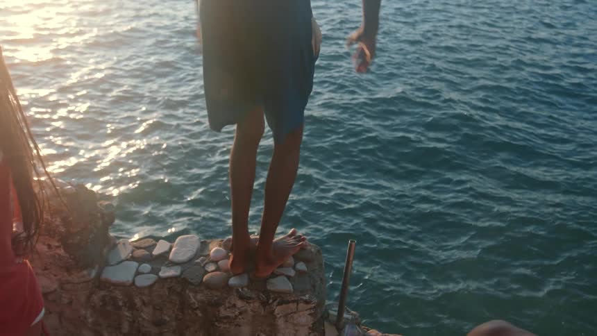 Person dives into the sea from a rocky ledge at sunset