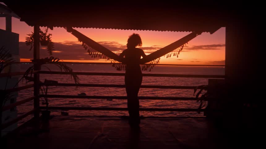 A woman stands on the terrace looking at the sunrise on the ocean