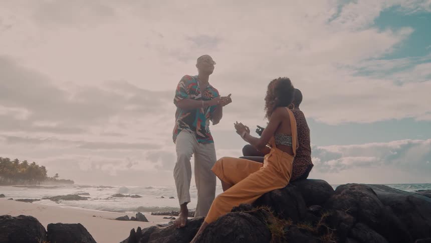 Three people on rocks in the sea clapping and dancing happily