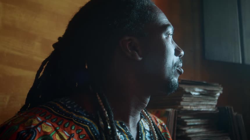 Man sitting near a stack of vinyl records stares out the window